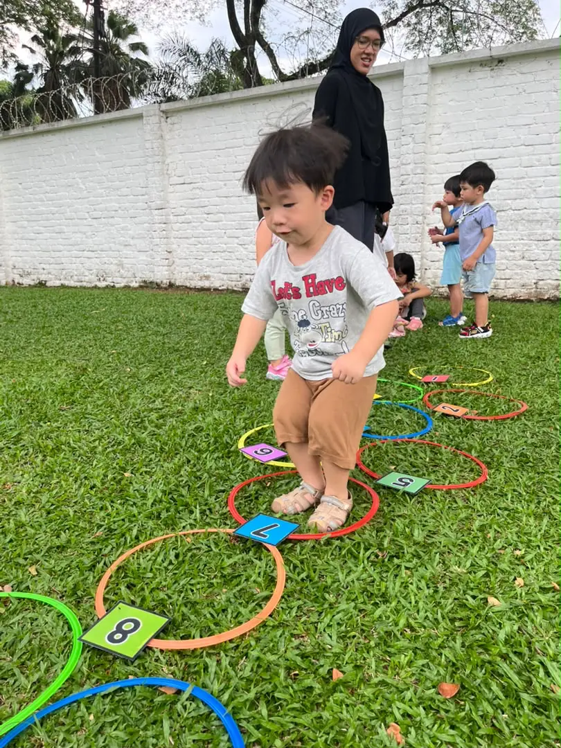 A boy hopping between rings on the grass of the outdoor play area