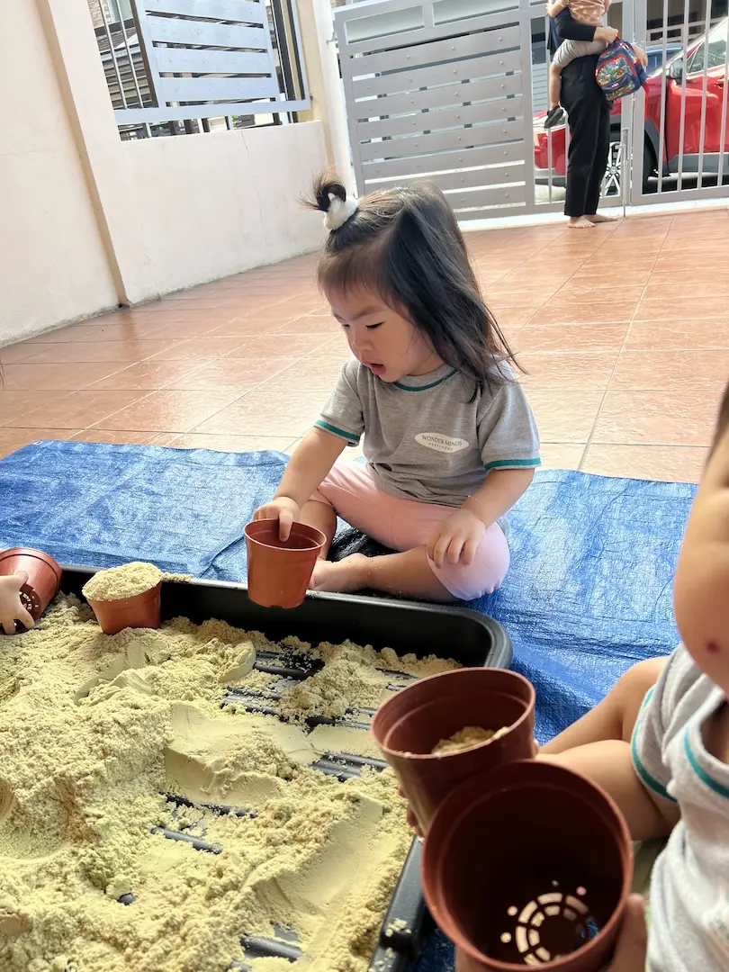 A toddler playing with sand and small flower pots in a sensory tray