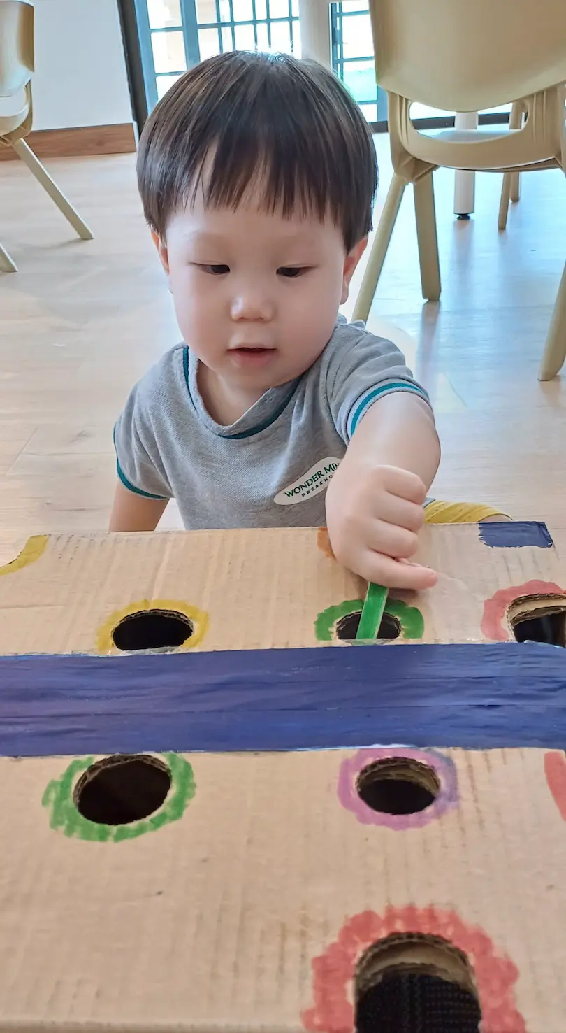 A child pushing a stick through holes in a painted cardboard box
