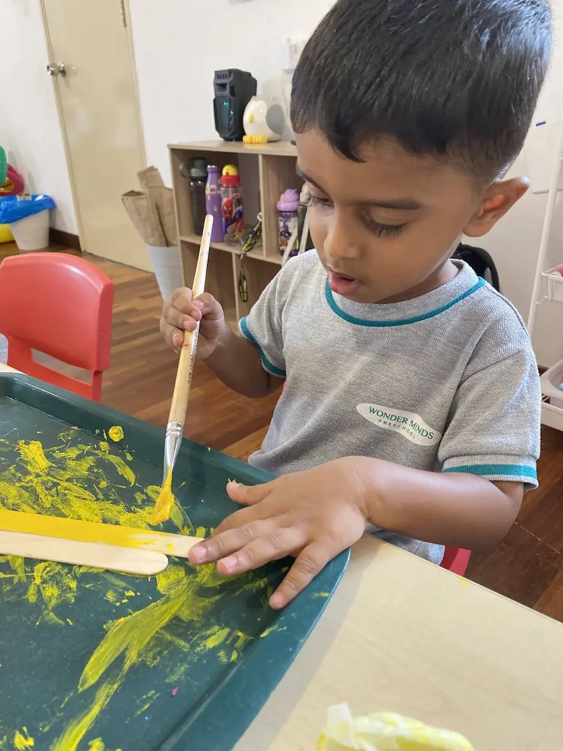A boy painting with yellow paint in a tray