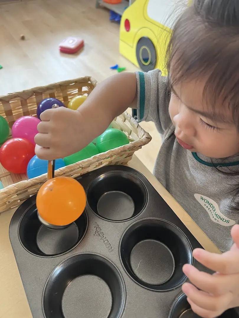 A girl placing coloured balls into a muffin tray