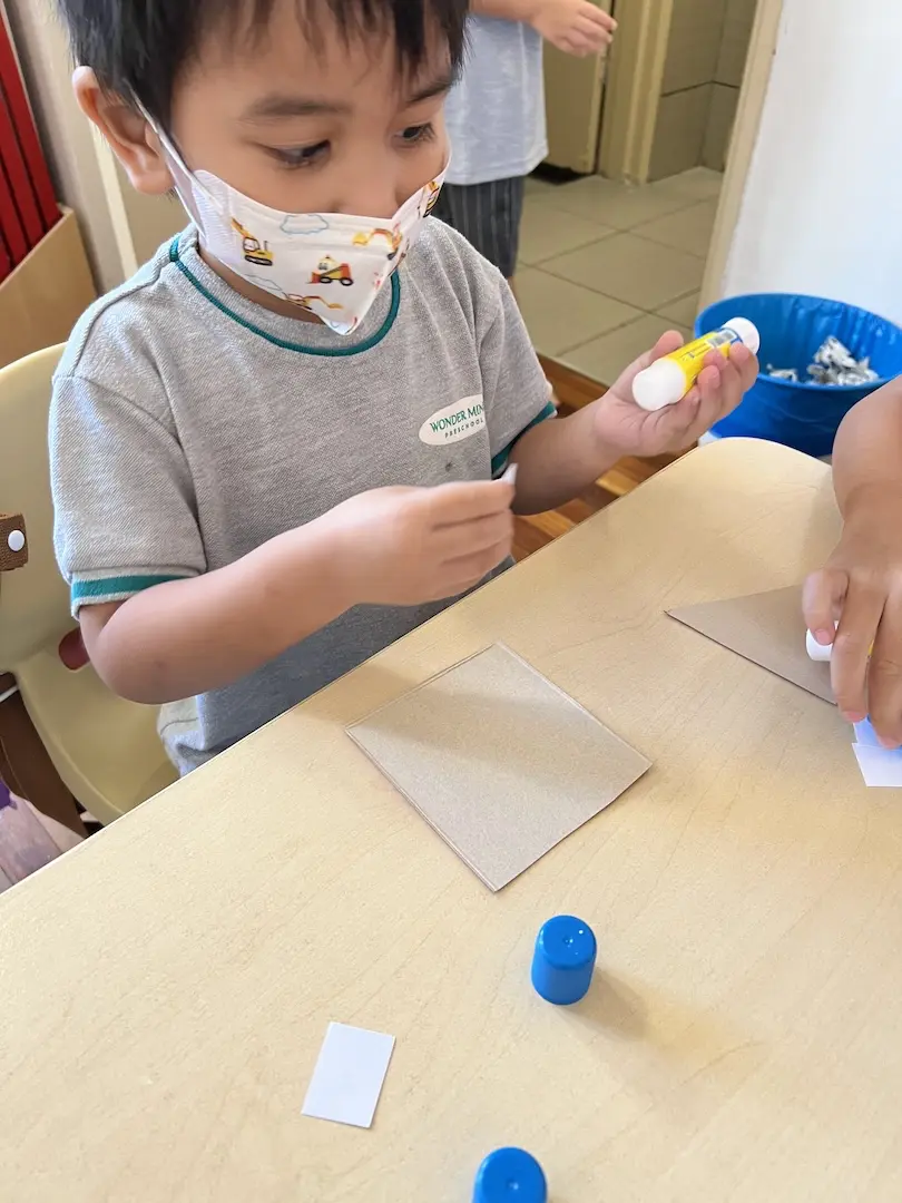 A boy holding a glue stick over cardboard
