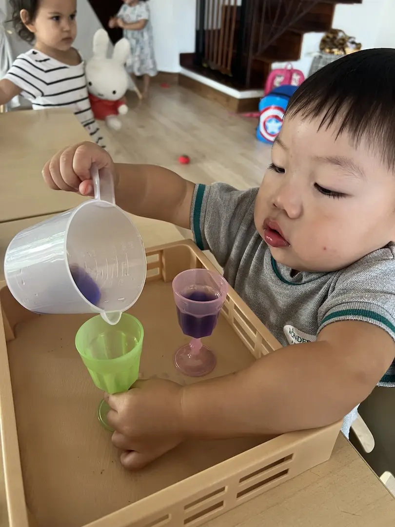 A boy pouring purple water between cups