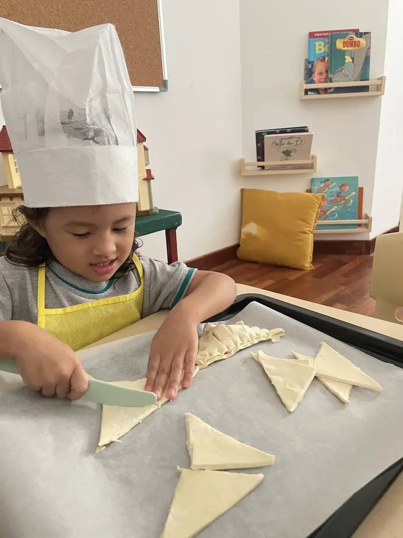 A girl in a chef hat cutting pastry dough