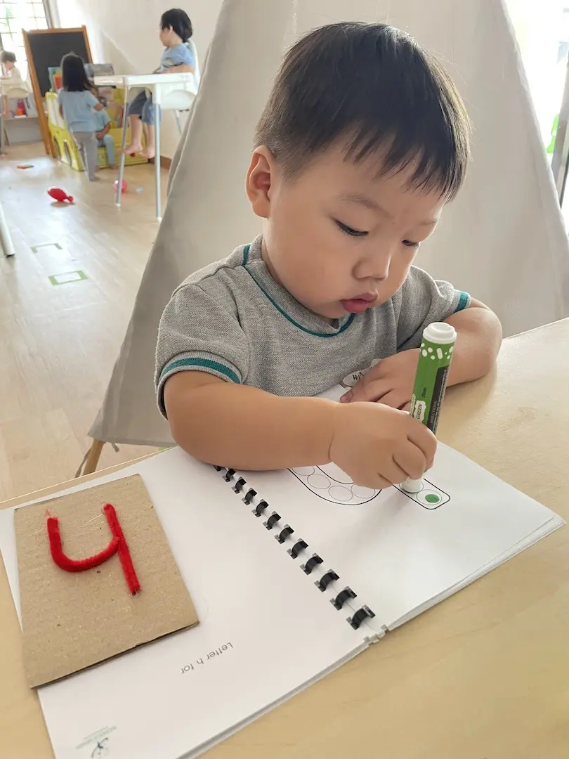 A boy colouring in a workbook beside a tactile letter