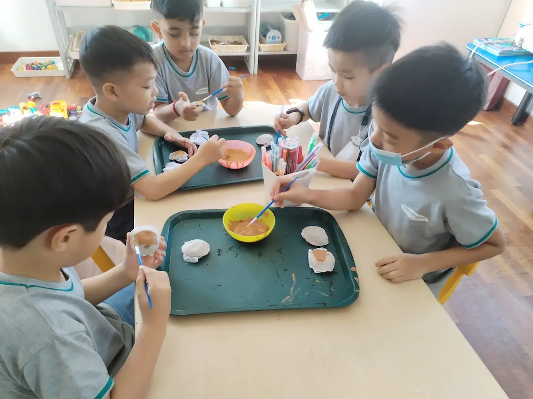 Children decorating small items with paint at a shared table