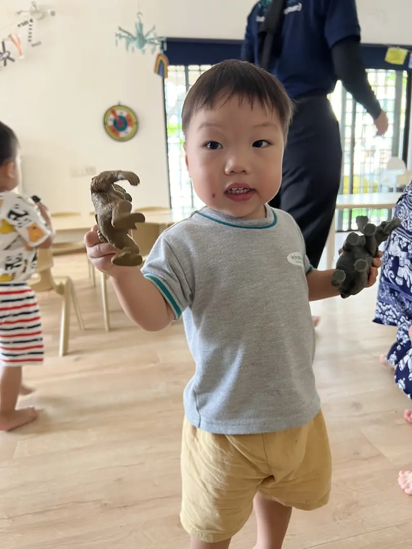 A boy holding two toy dinosaurs