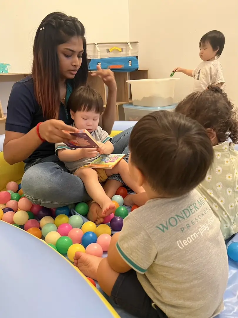 A teacher showing a picture book to toddlers in a ball pit
