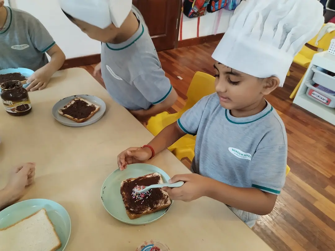 A boy in a chef hat spreading chocolate on toast