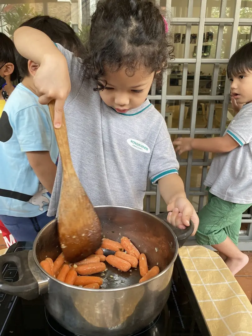 A child stirring a pot of carrots with a wooden spoon