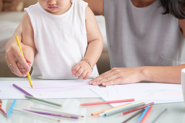 mother helping toddler colouring on a notebook